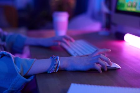 Armen van persoon zichtbaar achter computerscherm met één hand op de muis en één hand op het toetsenbord